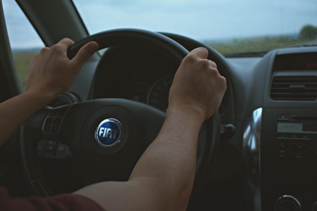 pexels photo 1405666 1405666 Close-up of hands on the steering wheel of a Fiat car interior, perfect for travel and automotive themes.